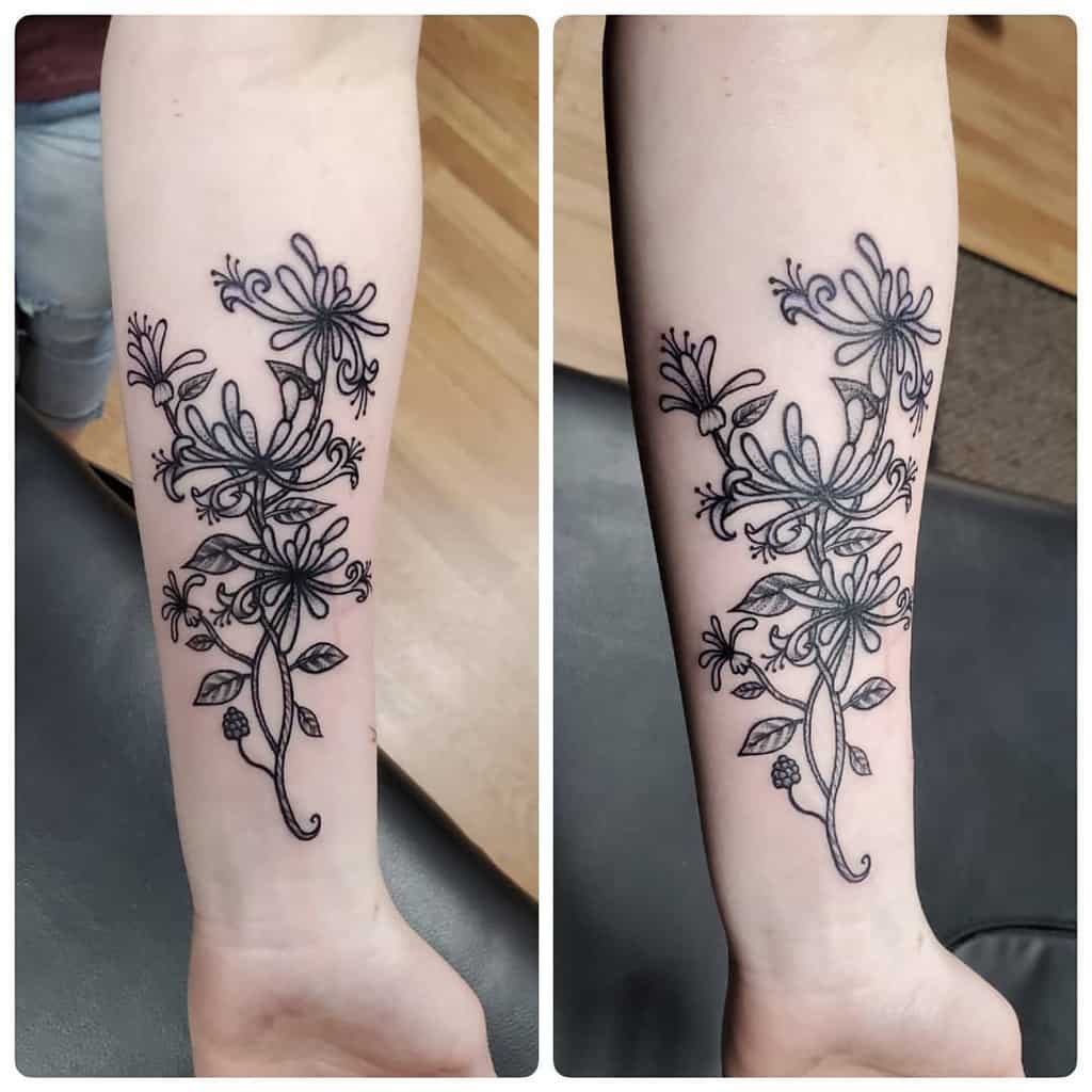 Dainty black ink honeysuckle tattoo on the forearm, featuring delicate flowers and leaves