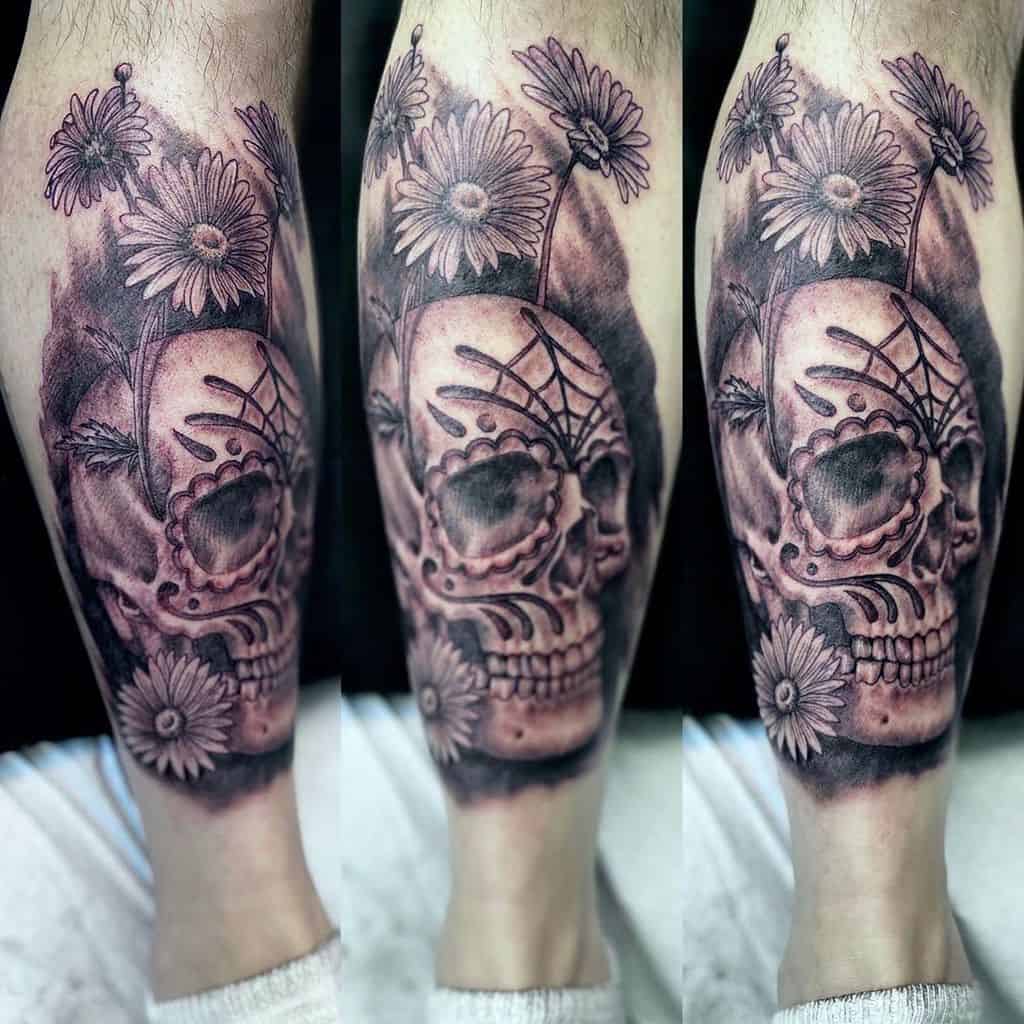 Calf tattoo realistic black and grey skull with Day of the Dead markings surrounded by daisies