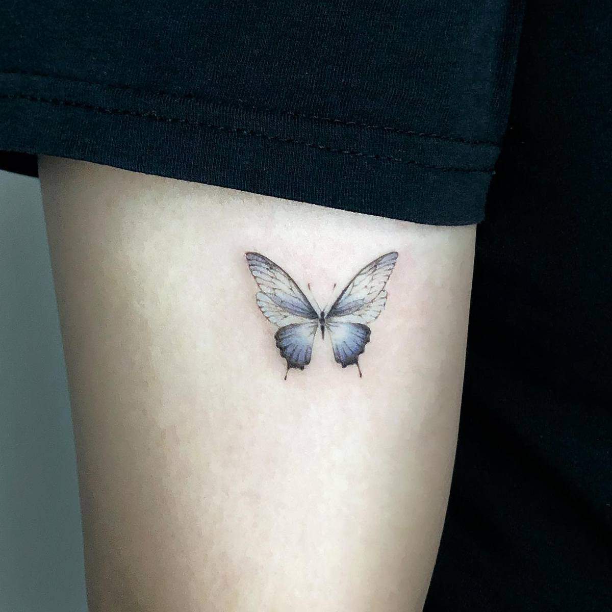A delicate, realistic butterfly tattoo on an upper arm