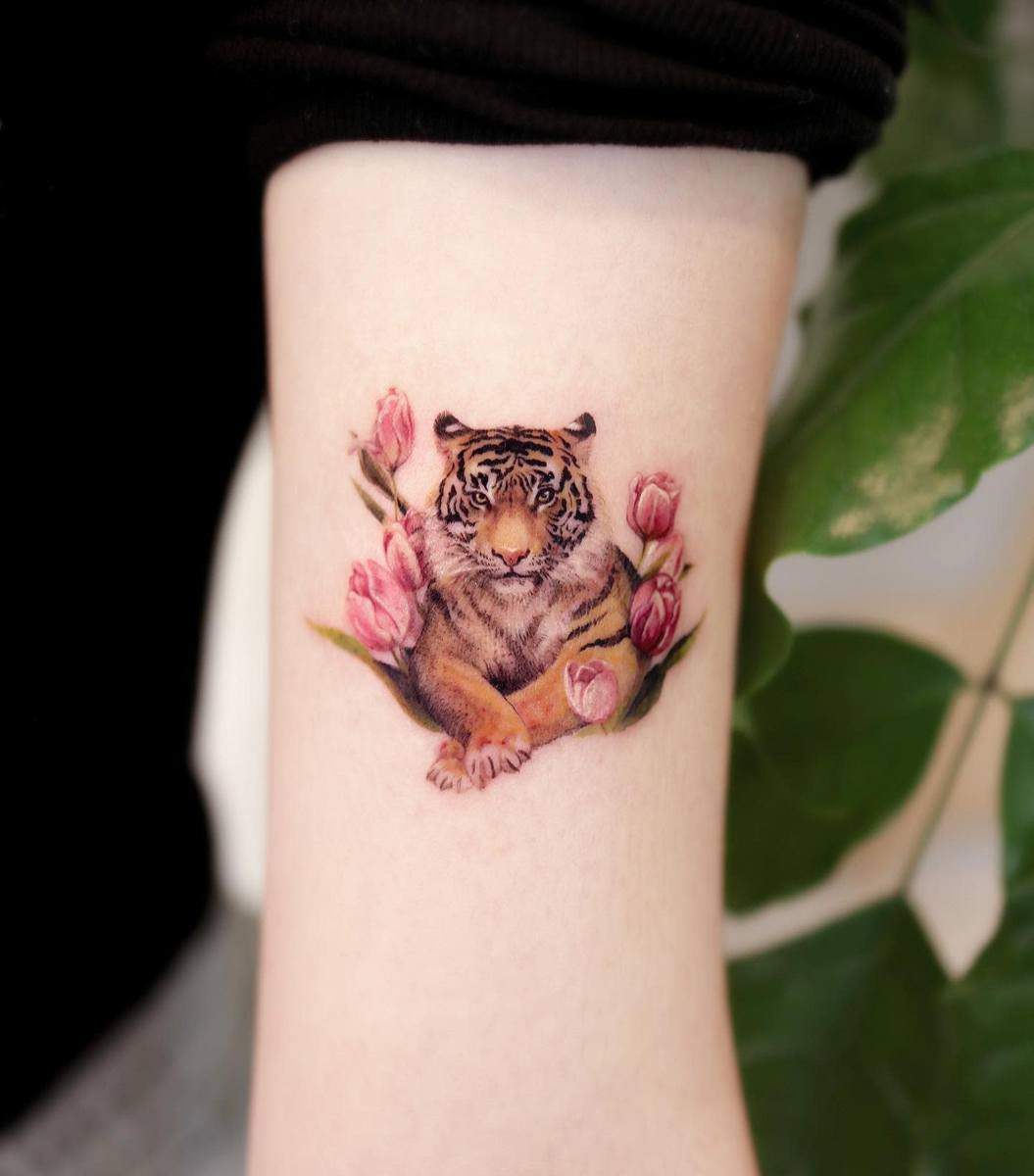 Tattoo of a tiger surrounded by pink flowers on a forearm