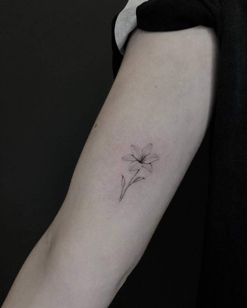 Minimalist fine-line tattoo of a small lily, featuring delicate detailing for an elegant and subtle floral design
