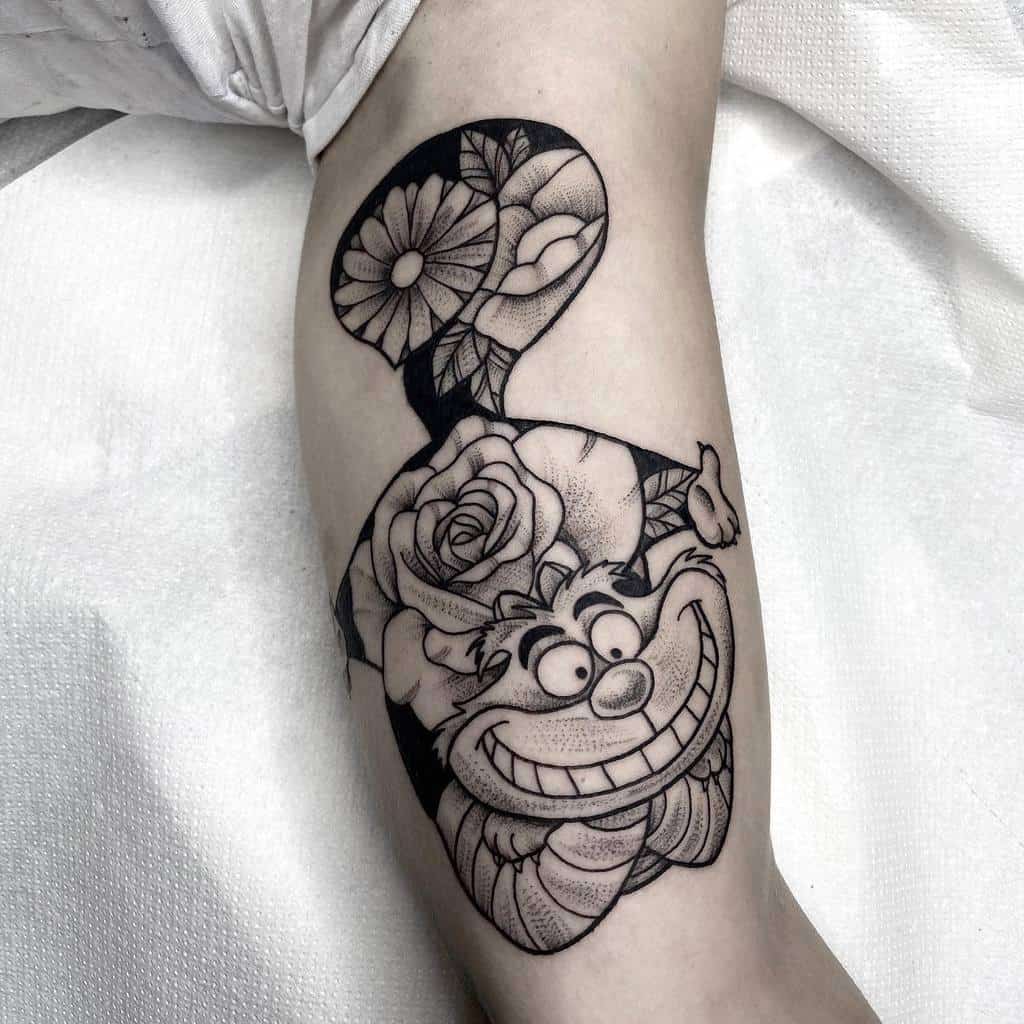 A black and grey Cheshire Cat tattoo featuring floral elements, with roses and daisies integrated into the design