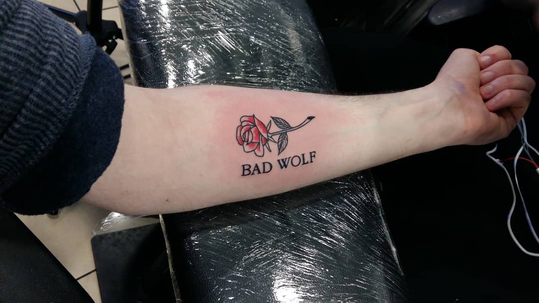 Simple and elegant Doctor Who tattoo featuring a red rose with the phrase 'BAD WOLF' underneath