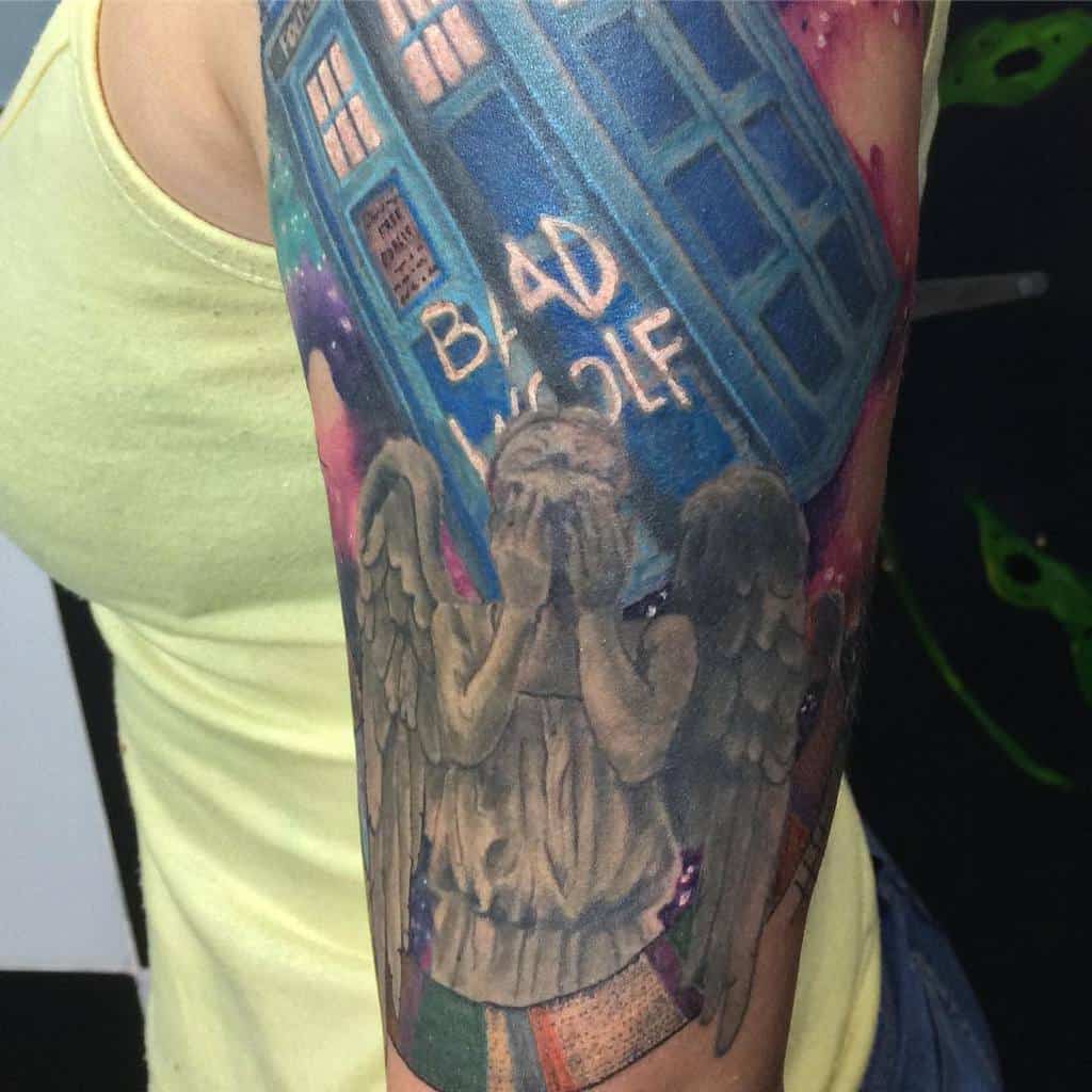 Colorful tattoo depicting a scene from 'Doctor Who' with the TARDIS, a Weeping Angel covering its face, and 'BAD WOLF' written on the TARDIS, set against a cosmic background