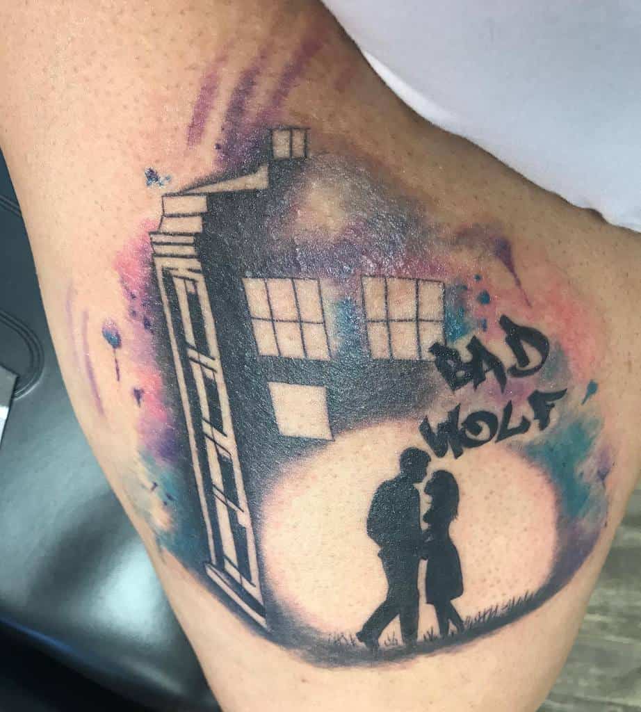 Vibrant tattoo depicting the TARDIS from 'Doctor Who' amidst a colorful cosmic backdrop, with a silhouette of a couple and 'BAD WOLF' graffiti