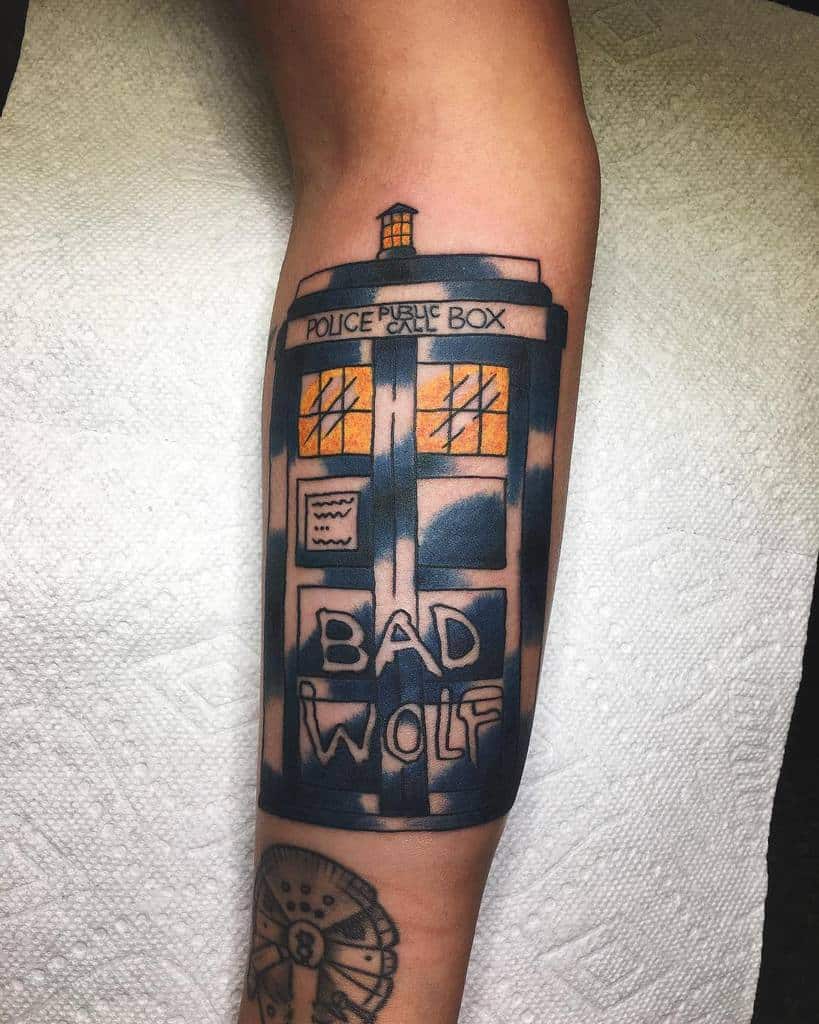 Bold tattoo of the TARDIS from 'Doctor Who' with illuminated windows, featuring 'BAD WOLF' prominently displayed across the door, inked in rich blue and black shades
