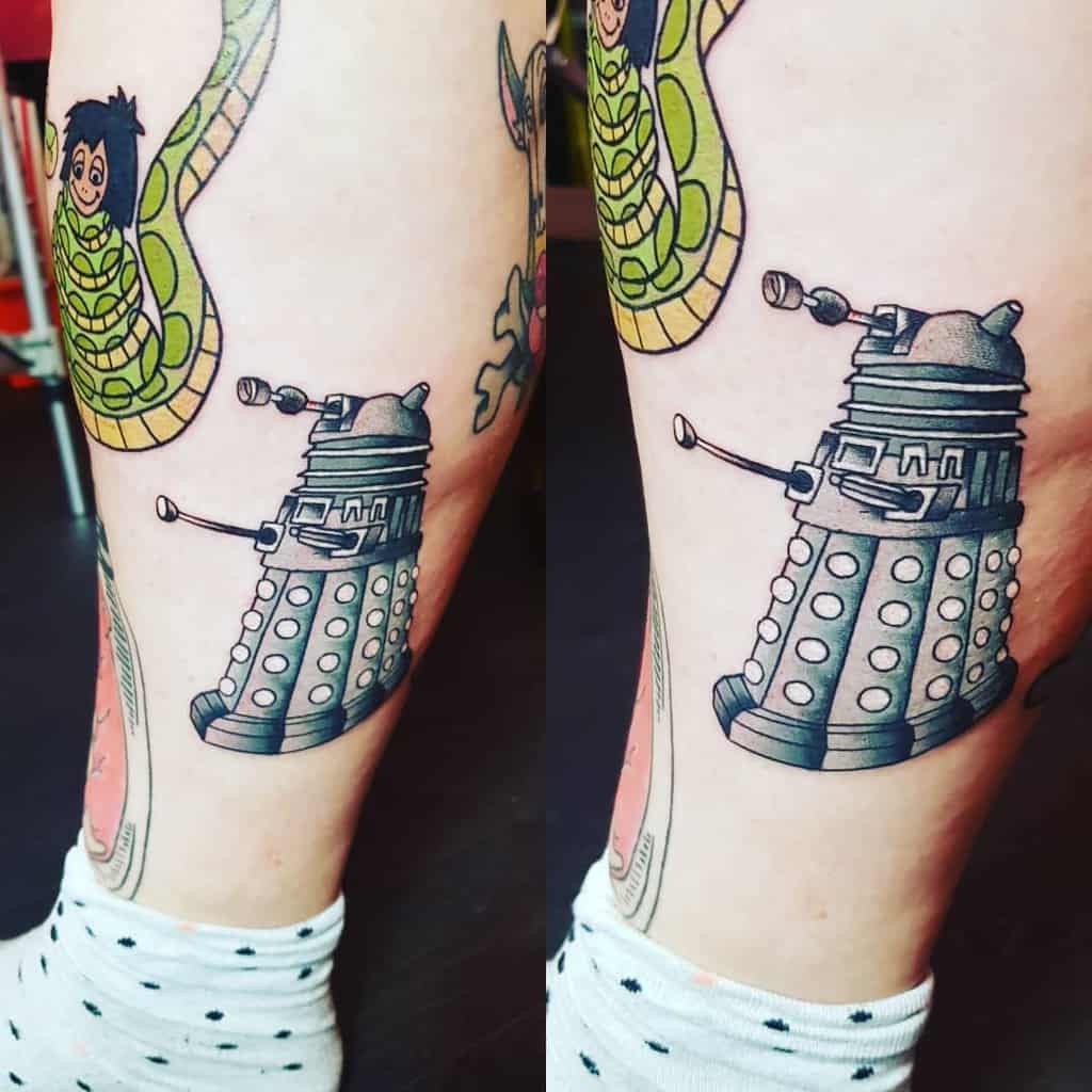 Creative tattoo featuring a Dalek from 'Doctor Who' in gray and blue tones, alongside a playful green serpent with a cartoon character's face