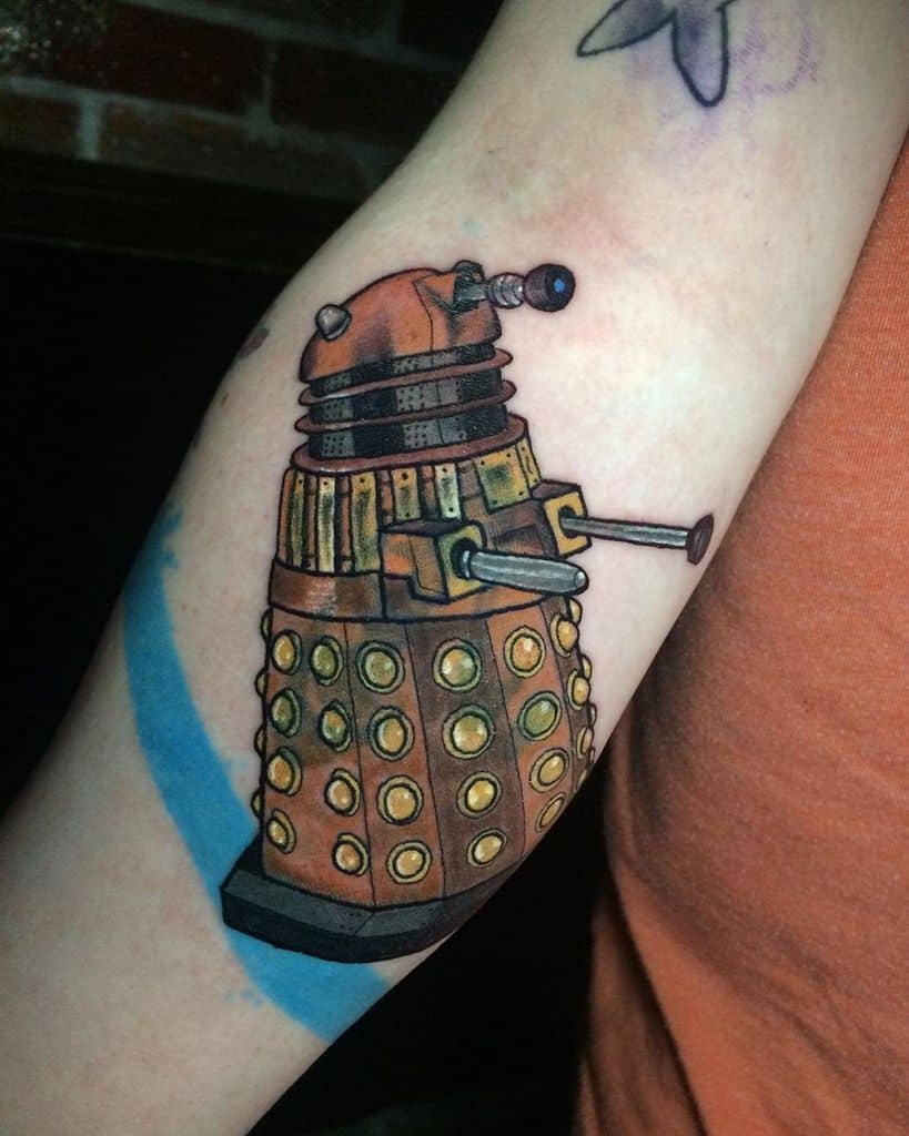 Detailed tattoo of a Dalek from 'Doctor Who', rendered in shades of orange and brown with highlighted metallic accents and dark shading