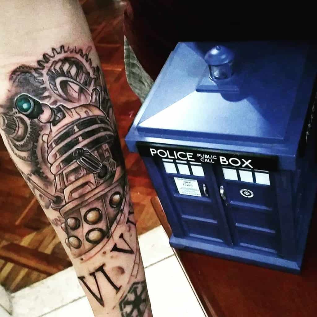 Intricate tattoo of a Dalek from 'Doctor Who', showcasing detailed mechanical components and gears gears with Roman numerals 'VI V IX' prominently displayed below