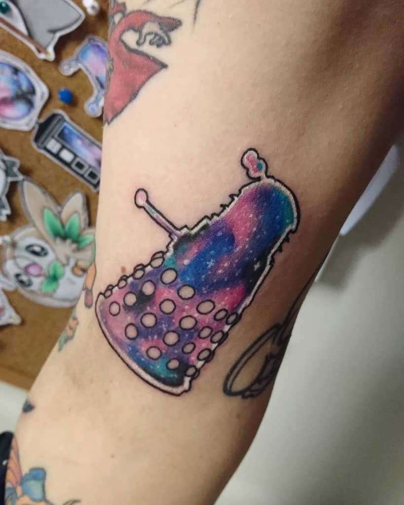 Colorful tattoo depicting a Dalek from 'Doctor Who', illustrated in a unique cosmic style with vibrant blues and pinks within the outline of the Dalek's silhouette