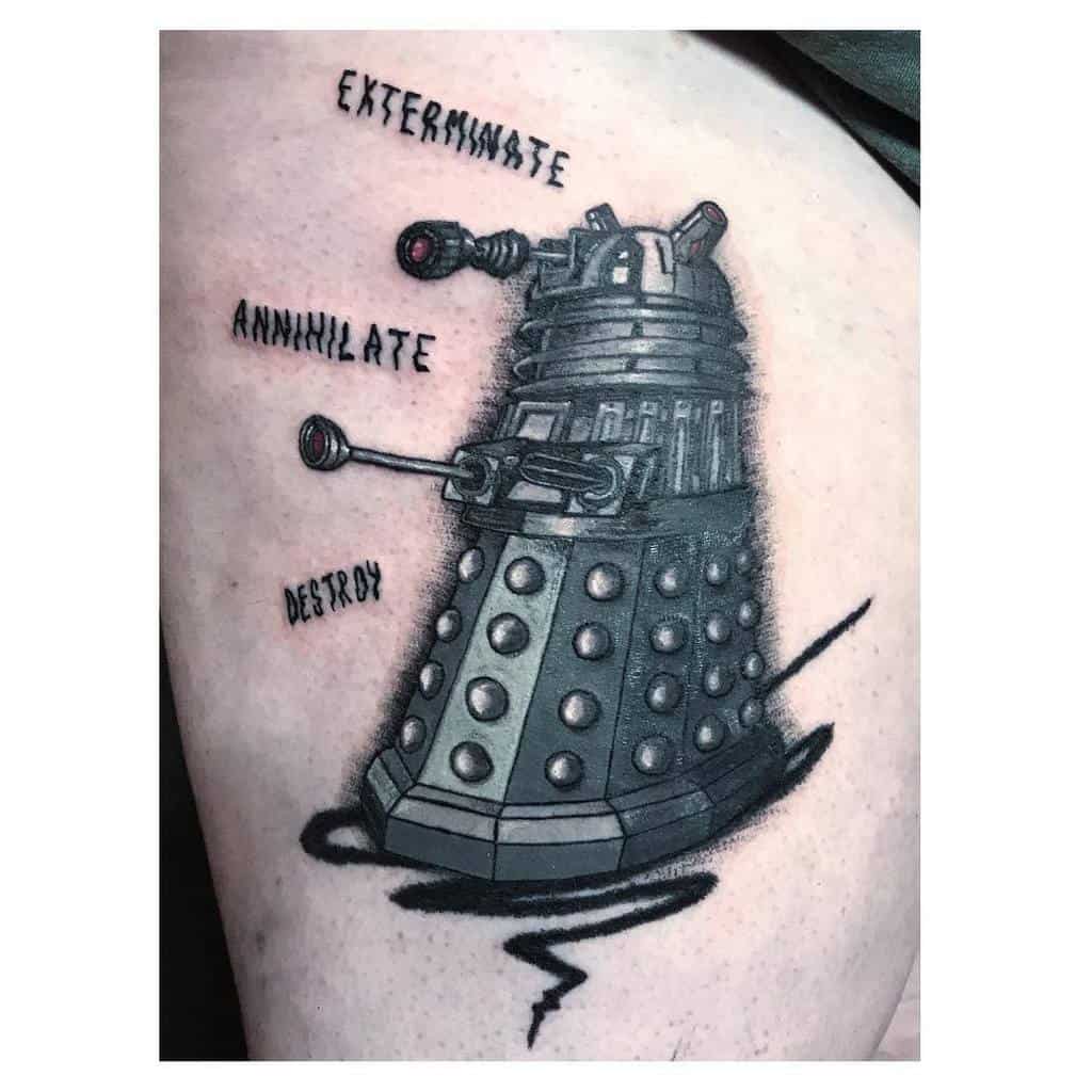 Striking black and grey tattoo of a Dalek from 'Doctor Who' on skin, detailed with the words 'EXTERMINATE', 'ANNIHILATE', and 'DESTROY' floating above and around it in bold, aggressive fonts