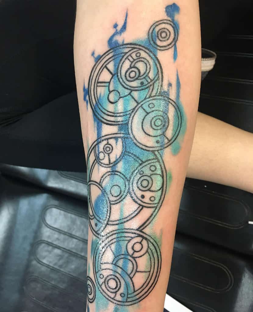 Elaborate tattoo featuring Gallifreyan script from 'Doctor Who', presented as a series of interconnected circles and loops, accented with splashes of blue and teal