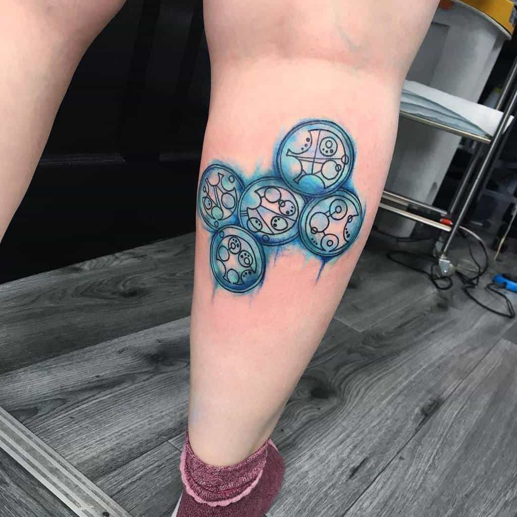 Colorful tattoo of 'Doctor Who' Gallifreyan symbols in a cluster, highlighted with shades of blue and teal