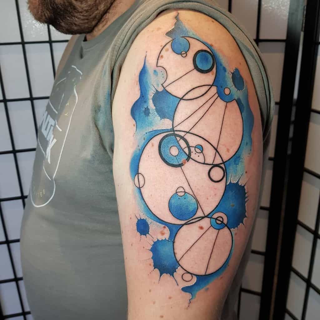 Colorful tattoo showcasing Gallifreyan script from 'Doctor Who', with swirling circles and abstract blue splashes