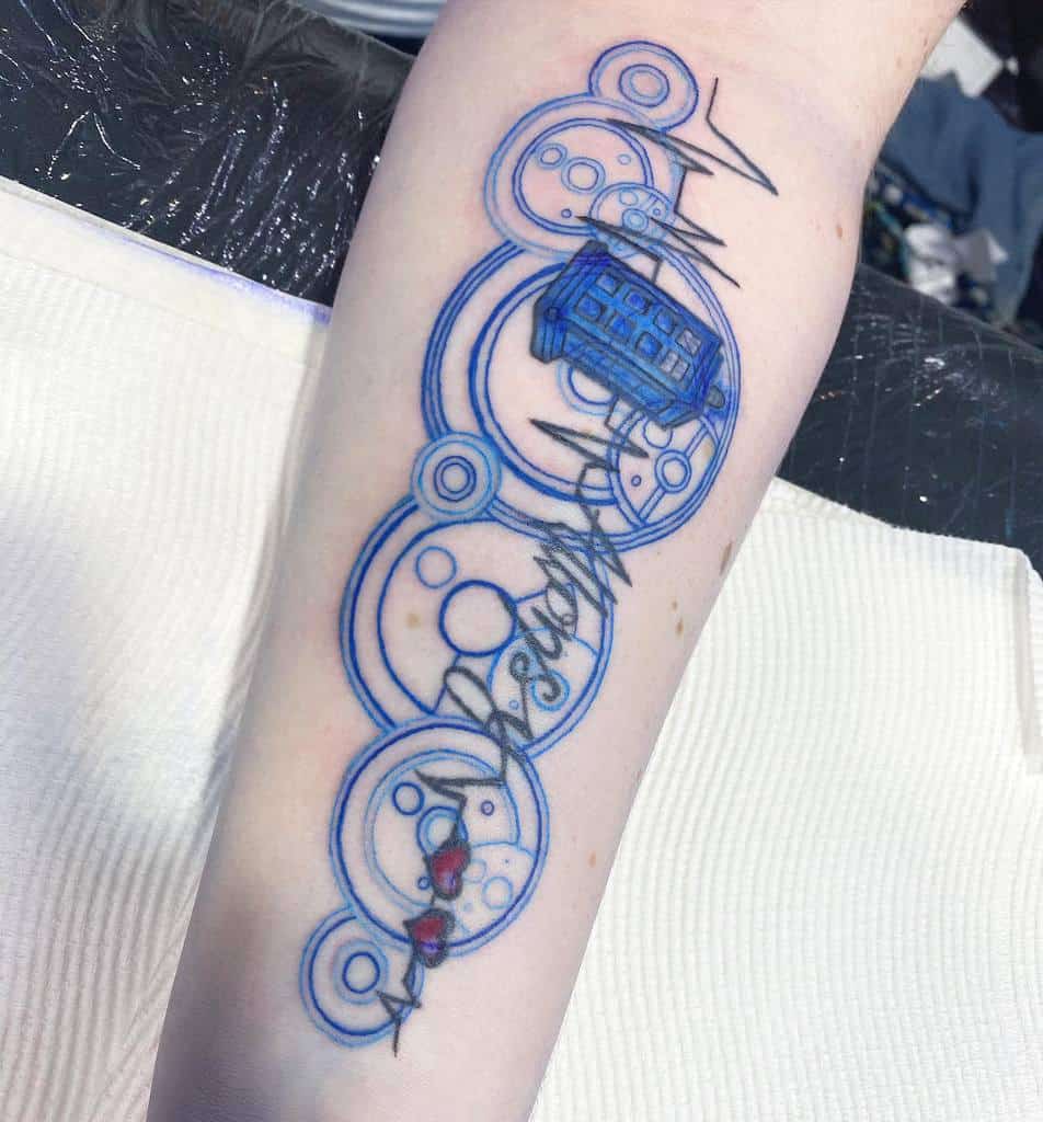Tattoo of Gallifreyan script from 'Doctor Who', featuring a TARDIS, abstract circles in blue, and a heartbeat line with two red hearts