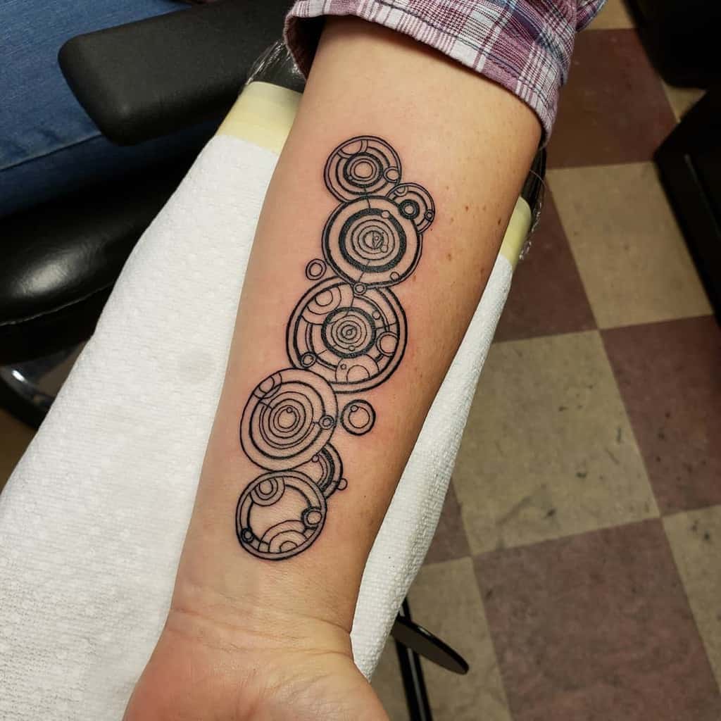 Tattoo showcasing a vertical sequence of Gallifreyan script from 'Doctor Who', featuring intricate circular patterns and fine line detailing