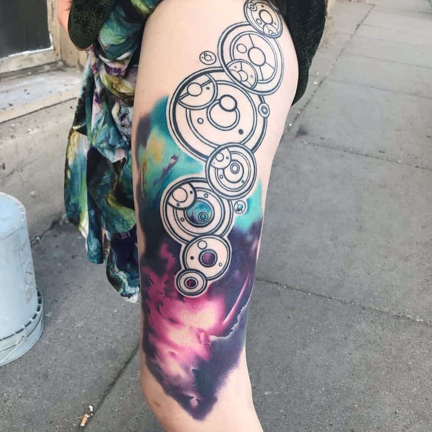 Vibrant tattoo of Gallifreyan script from 'Doctor Who', with intricate circular symbols set against a colorful, watercolor-style background blending blues and purples