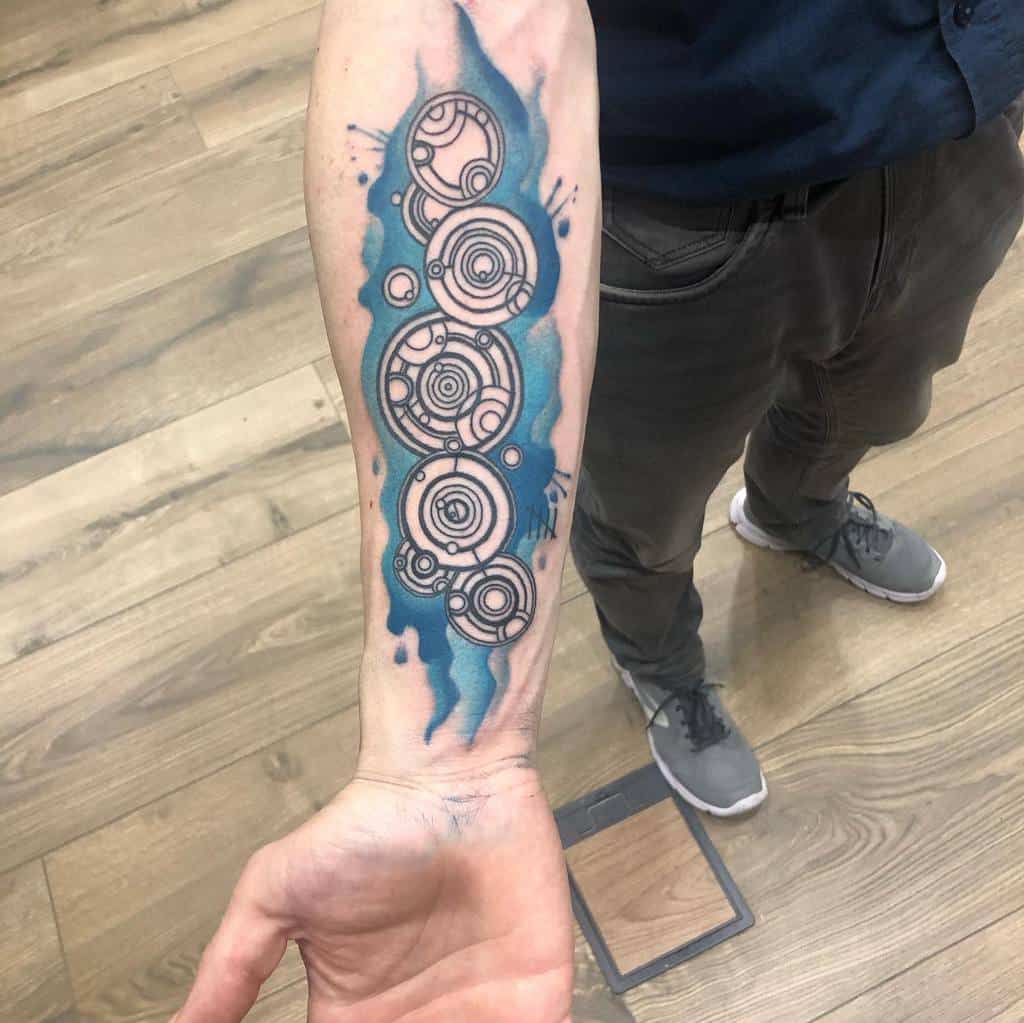 Striking tattoo of Gallifreyan script from 'Doctor Who', composed of elaborate circular designs with vibrant blue splashes