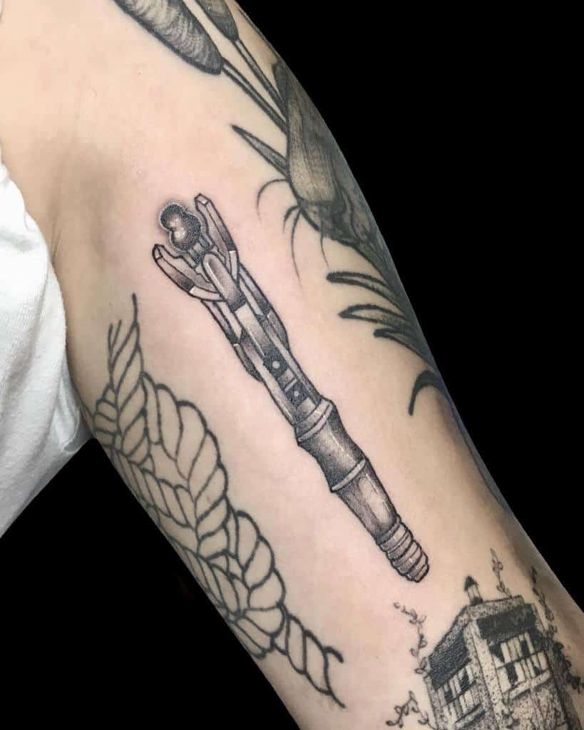 Elegant black and grey Doctor Who tattoo of a Sonic Screwdriver, inked among botanical designs and detailed foliage