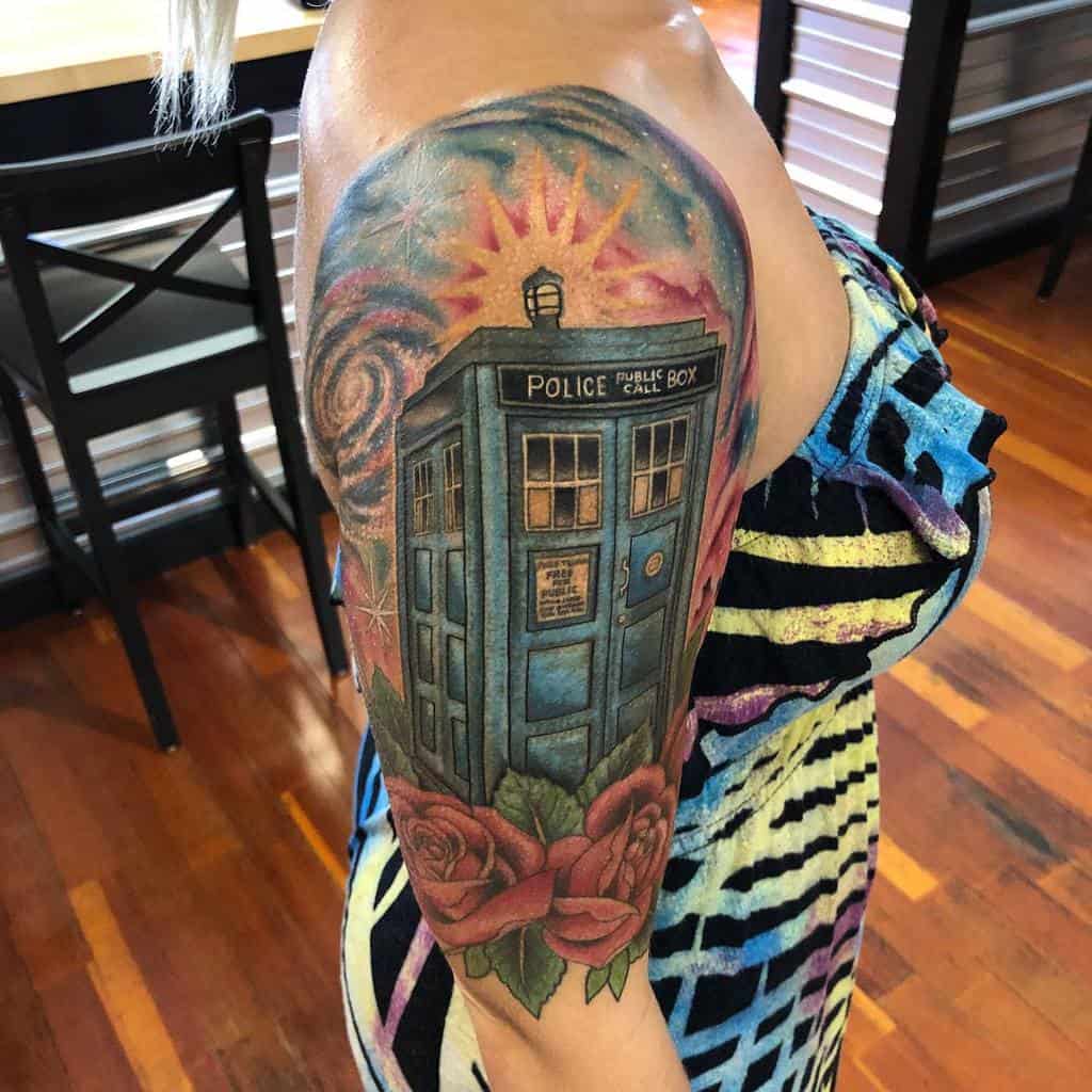 Vibrant Doctor Who tattoo, depicting the TARDIS with a radiant sunburst behind it and surrounded by red roses and cosmic swirls