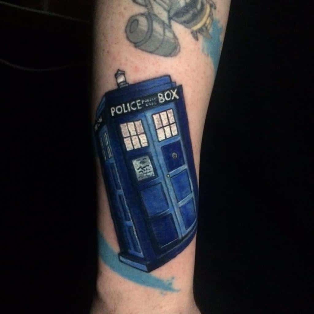 Doctor Who tattoo featuring a dark blue TARDIS with light accents, with a faded image of a Cyberman's head in the background