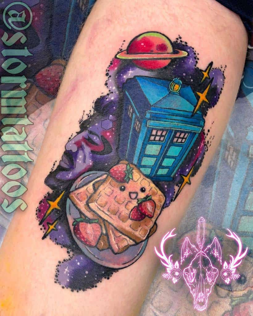 Colorful and whimsical Doctor Who tattoo featuring the TARDIS in a cosmic setting with a smiling waffle, strawberries, and planets