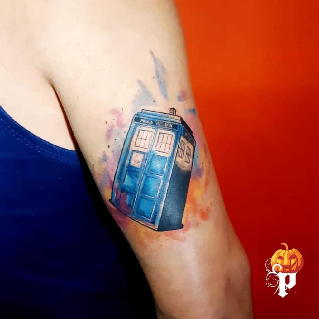 Doctor Who tattoo featuring the TARDIS with a vibrant watercolor background in shades of blue, orange, and pink