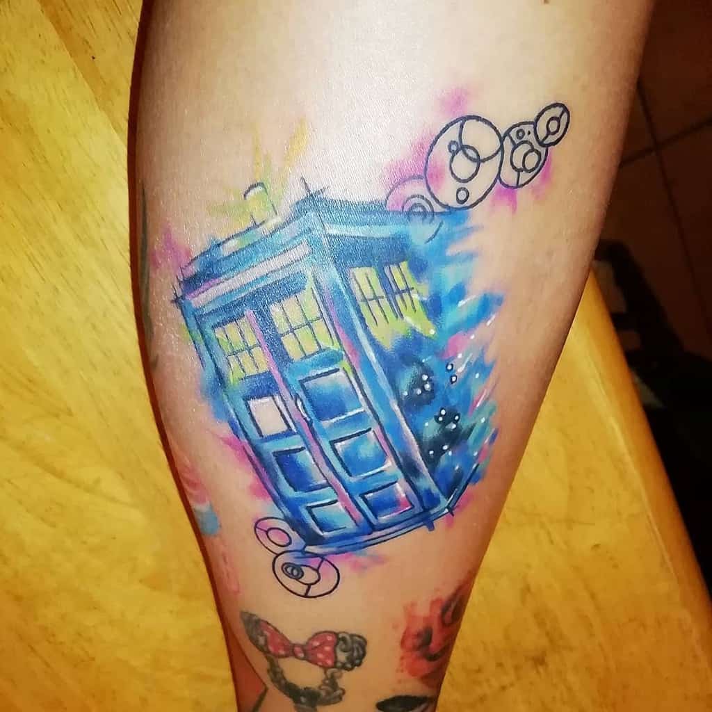 Doctor Who tattoo featuring the TARDIS in a vibrant watercolor explosion of blues, pinks, and yellows, with Circular Gallifreyan symbols