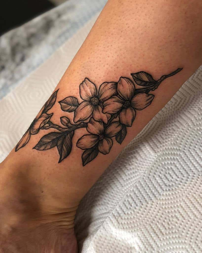 A black and gray tattoo of blooming dogwood flowers and leaves elegantly adorns a lower leg