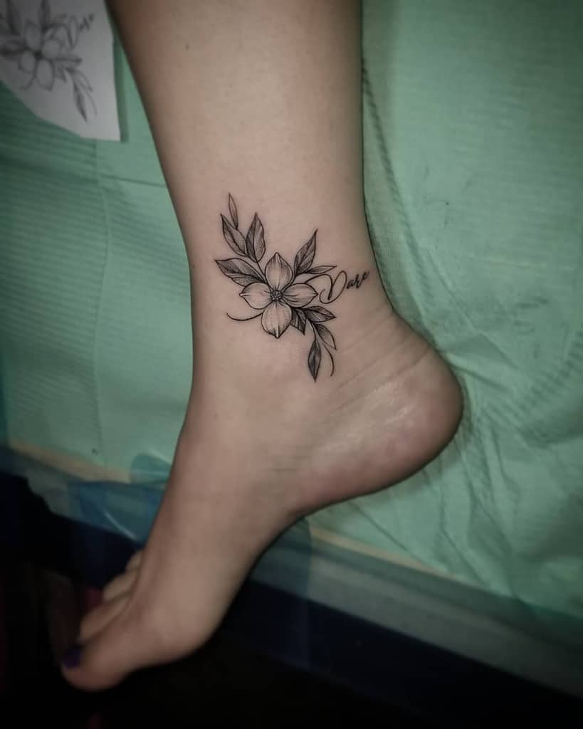 Ankle adorned with a floral tattoo showcasing delicate dogwood leaves and a blossom