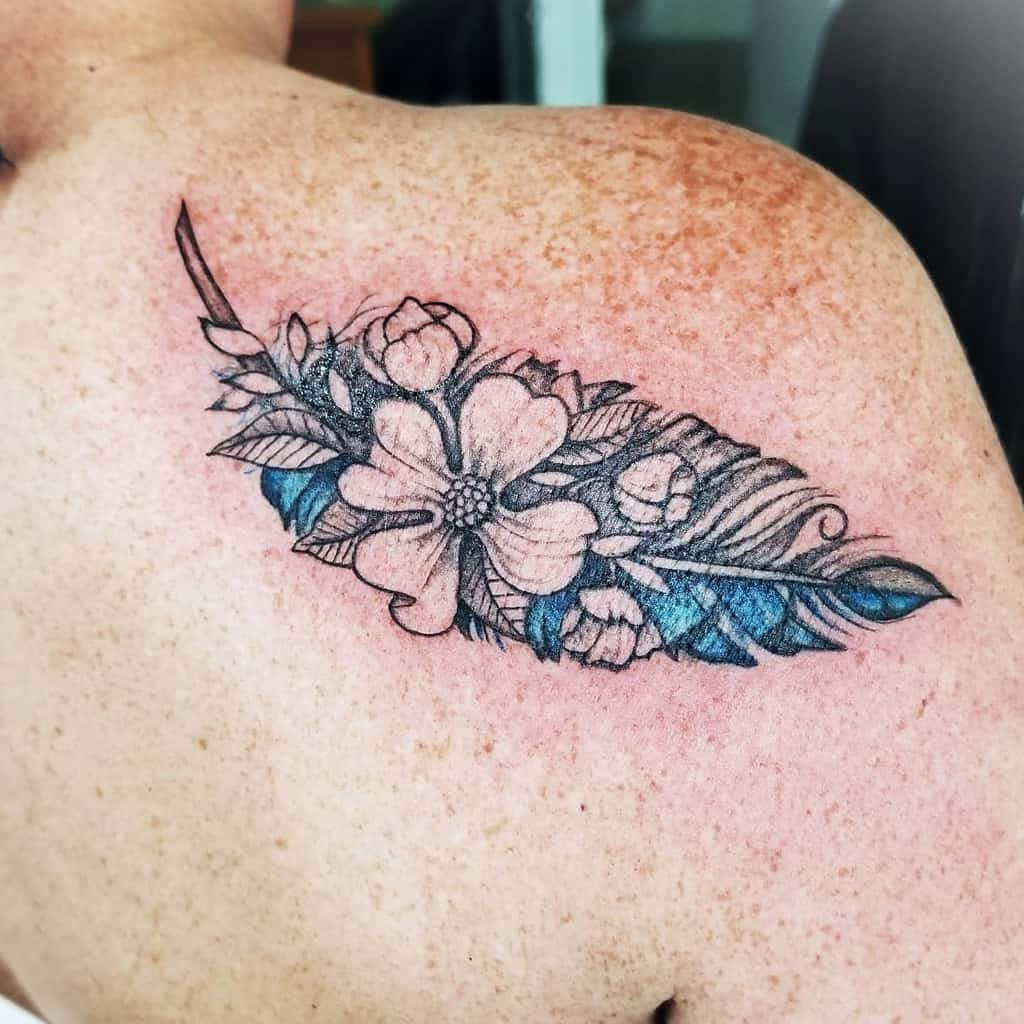 Tattoo of a feather filled with dogwood flowers and leaves gracefully inked on a person's shoulder