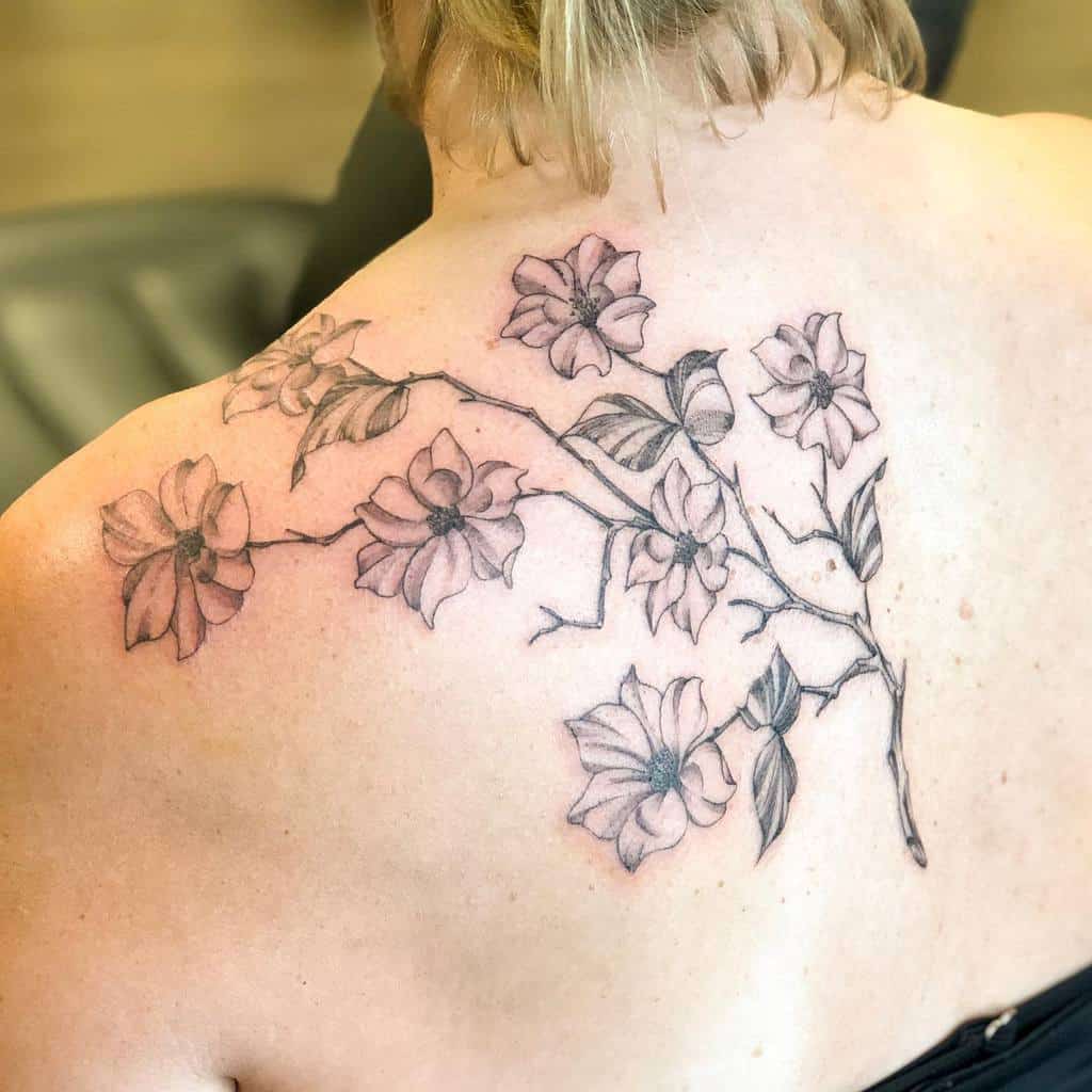 A delicate floral tattoo featuring pink dogwood flowers and lush green leaves graces the person's upper back