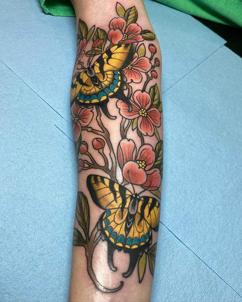 Forearm tattoo of butterflies and pink dogwood flowers with green leaves