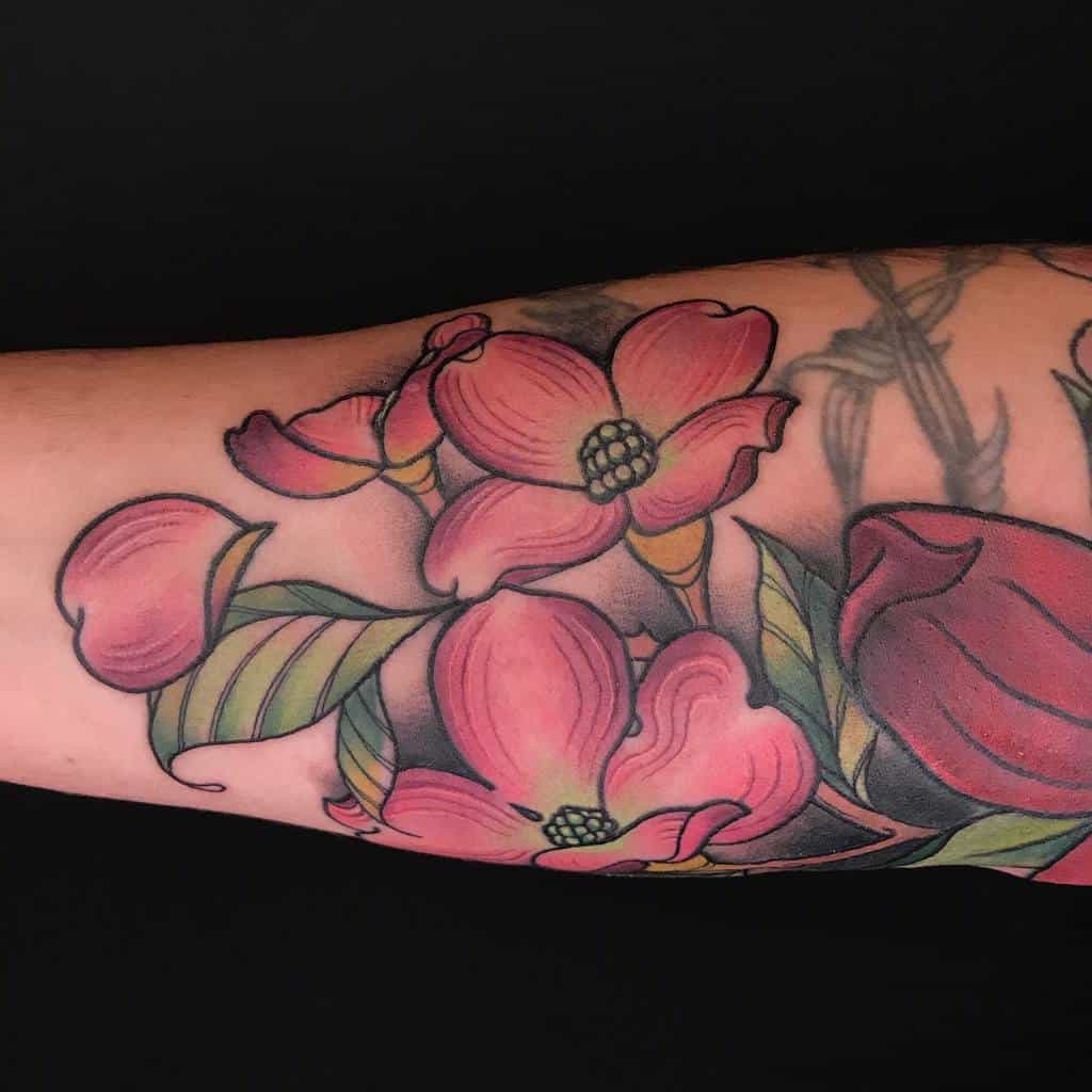 Tattoo of delicate pink dogwood flowers and lush green leaves on an arm