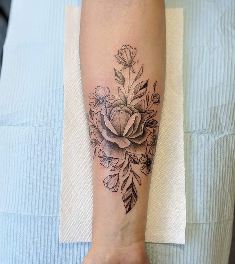Delicate black and grey tattoo of a large rose with surrounding smaller dogwood flowers and leaves, placed on the forearm