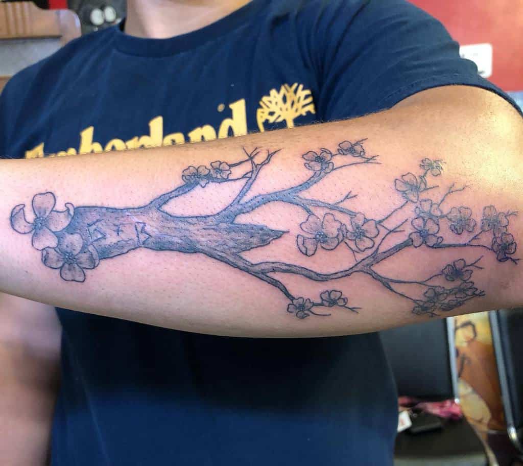 A person's arm features a tattoo of a flowering dogwood branch, elegantly extending across the skin