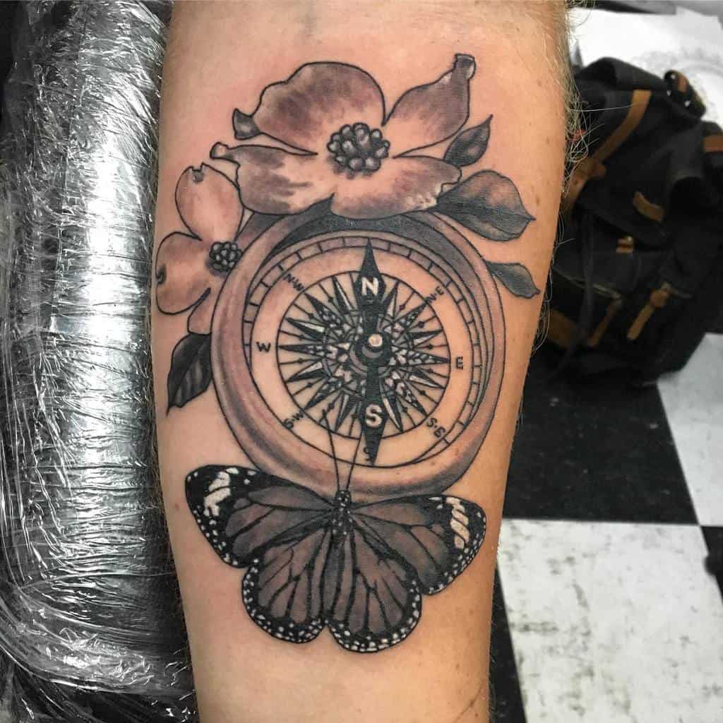 A tattoo of a compass with cardinal points, beautifully entwined with dogwood flowers and graced by a butterfly