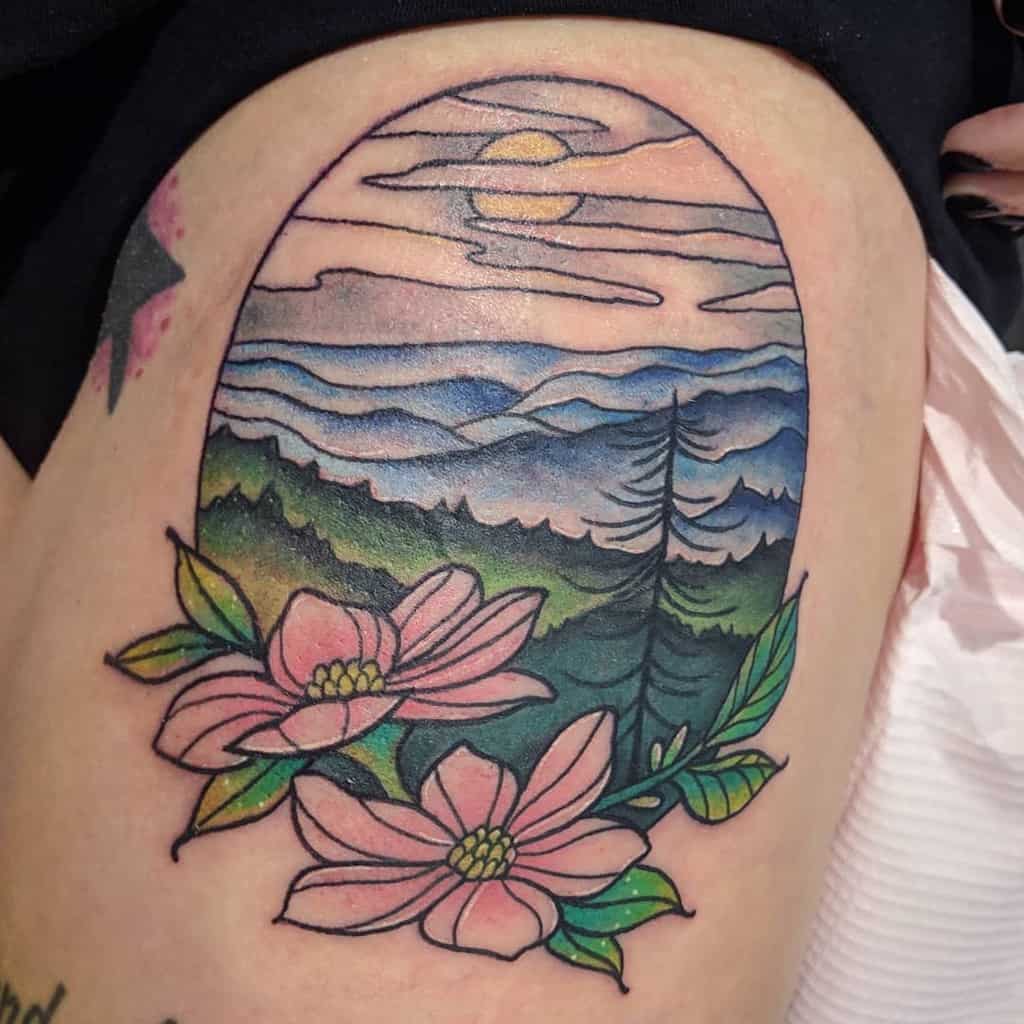 Tattoo of a scenic landscape with majestic mountains, a radiant sun, and two delicate pink dogwood flowers in the foreground
