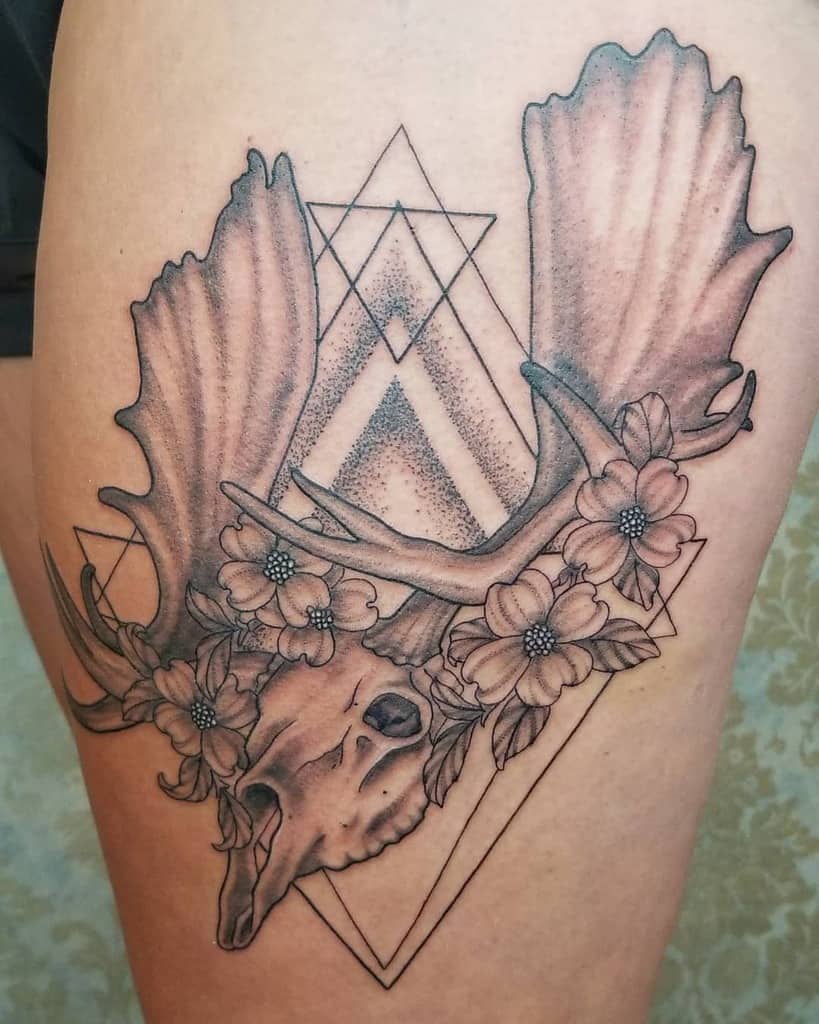 Tattoo of a deer skull adorned with dogwood flowers and intricate geometric shapes on the upper leg
