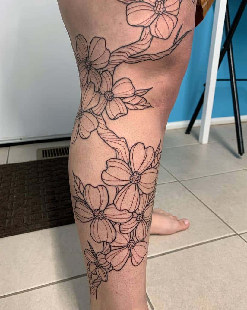 A dogwood floral outline tattoo graces a person's leg, featuring interconnected blossoms and branches