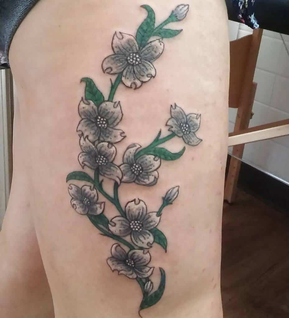 A dogwood tattoo featuring detailed blossoms and green leaves gracefully adorns a thigh