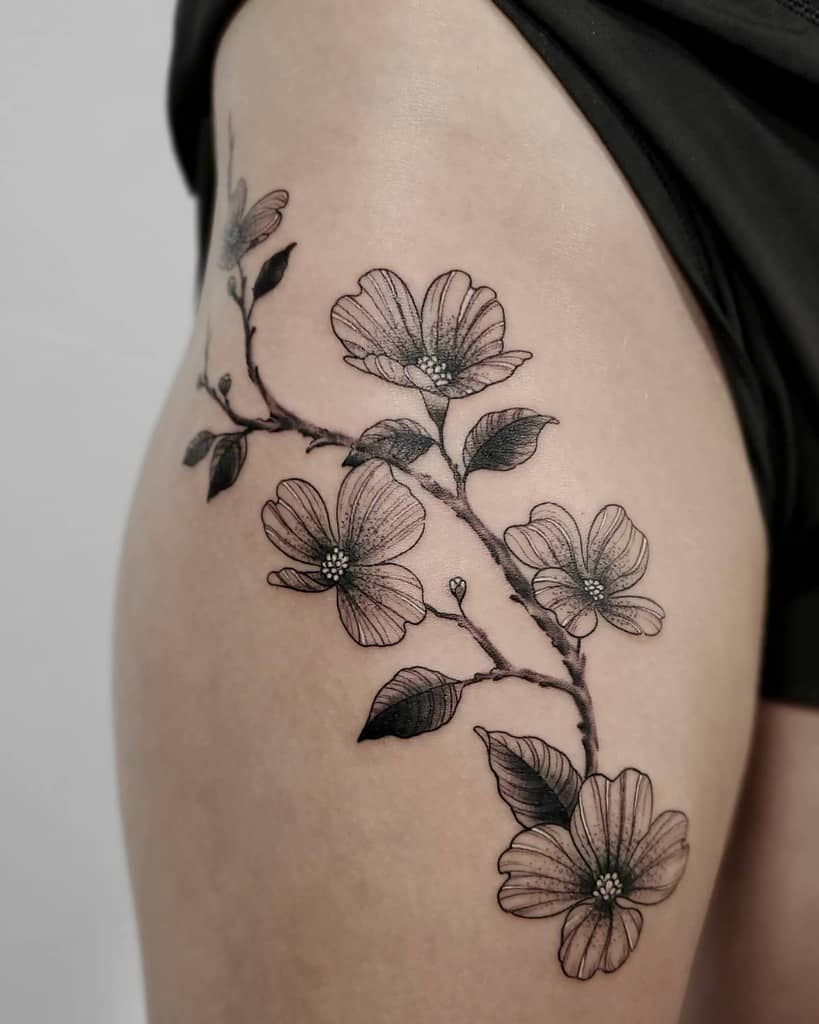 A thigh tattoo of a delicate dogwood branch with blooming flowers and leaves
