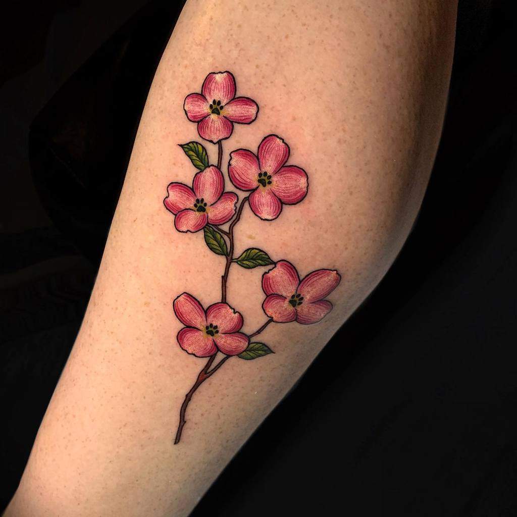 A tattoo of a pink dogwood floral branch with vibrant green leaves graces the leg