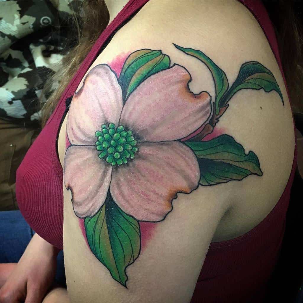 Tattoo of a large pink dogwood flower with lush green leaves gracing a woman's upper arm