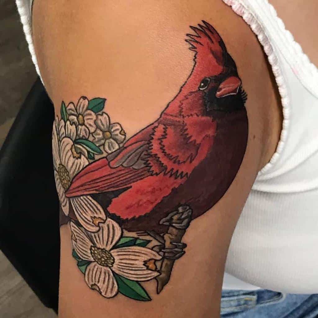 Vibrant tattoo of a red cardinal perched on a branch with white dogwood flowers, located on the upper arm