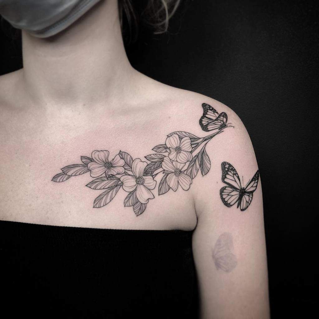 A woman with a tattoo of dogwood flowers and butterflies gracefully adorning her shoulder and collarbone
