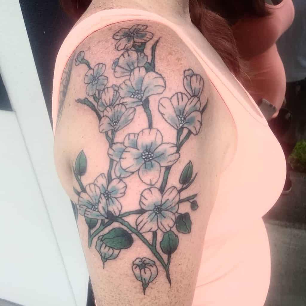 Detailed tattoo of blooming dogwood flowers with green leaves, covering the upper arm and shoulder