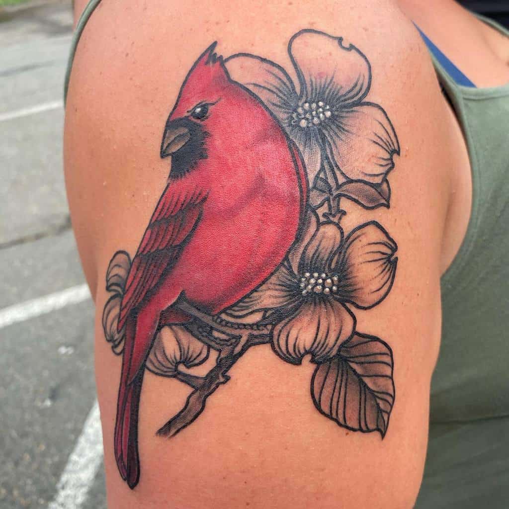 Vibrant tattoo of a red cardinal perched on a branch with detailed black and grey dogwood flowers, placed on the upper arm