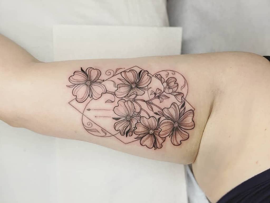 A floral tattoo featuring outlined dogwood flowers intertwined with geometric shapes graces an upper arm