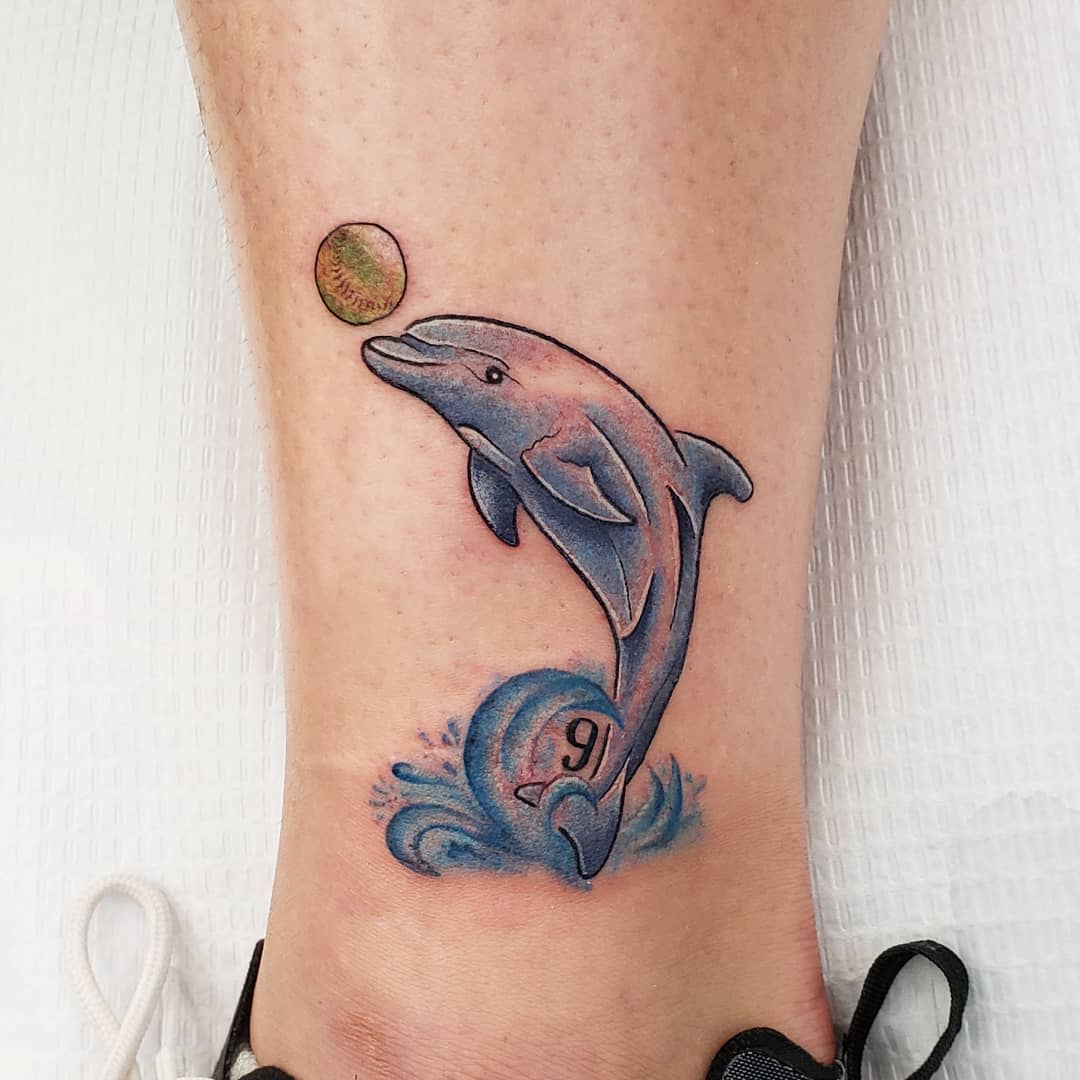 Tattoo of a dolphin playing with a ball on the left ankle